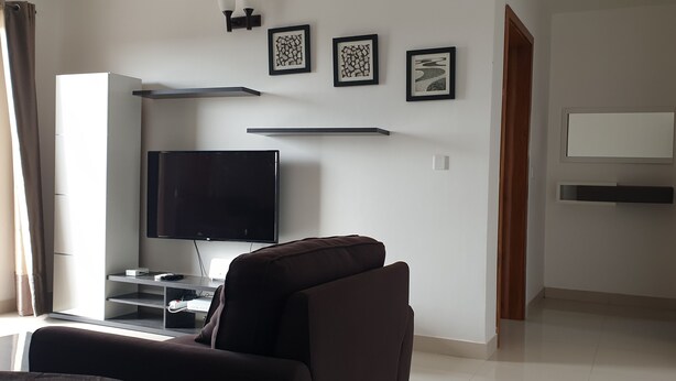 Ein modernes Wohnzimmer mit Flachbildfernseher, einer Couch, einem Couchtisch und einem TV-Schrank. An der Wand hängen drei gerahmte Kunstwerke, und eine Tür führt in einen anderen Raum.