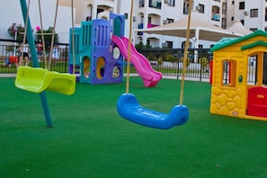 A playground with swings, a slide, and a small playhouse. - Seagull Hotel Apartments (Paralimni)