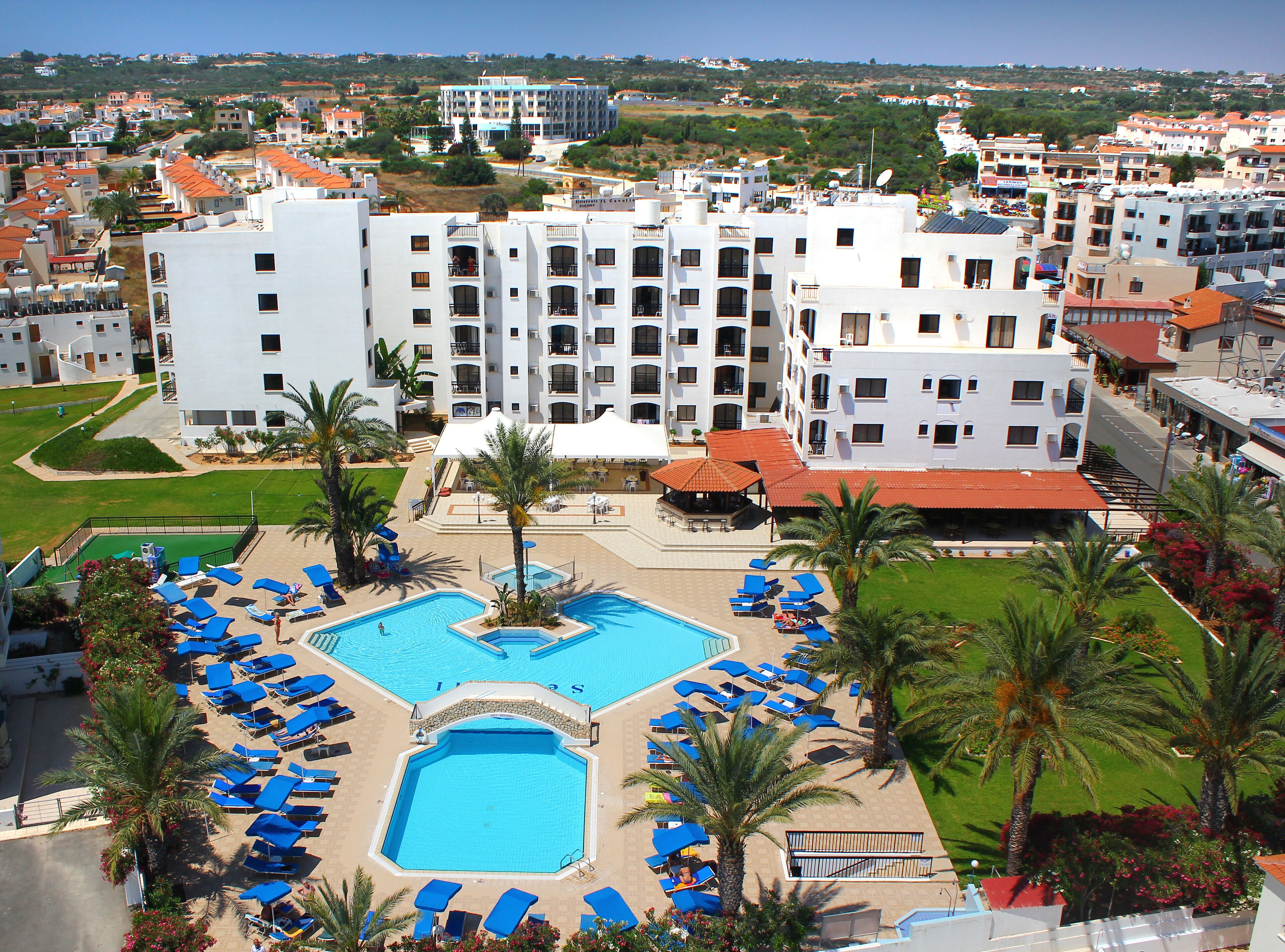 Un hotel con piscina central rodeada de tumbonas y palmeras, con vistas a la zona residencial circundante.