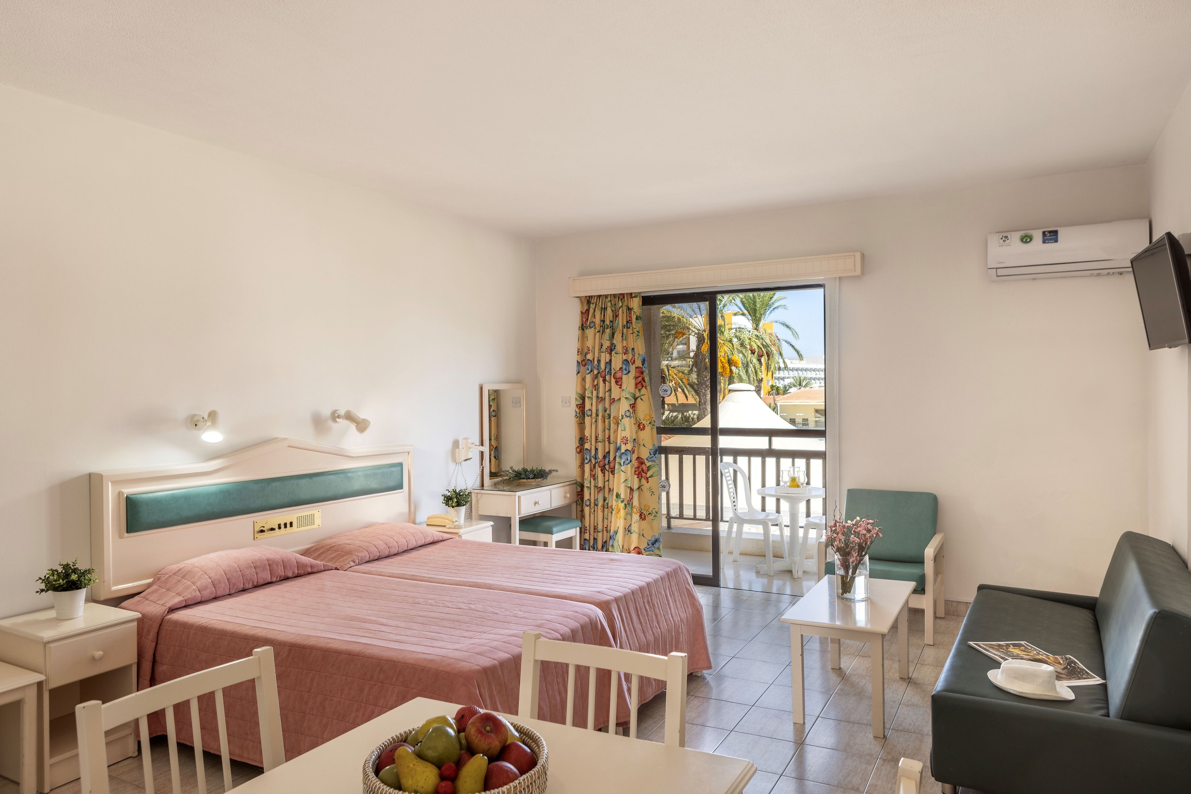 Une chambre d’hôtel comprenant un lit, un bureau, une chaise, un canapé et un balcon avec vue sur les palmiers.