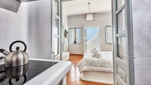 Une pièce compacte comprenant un coin cuisine, un lit et une vue sur le ciel par des portes ouvertes.