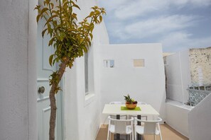 Une pièce aux murs blancs, avec une petite table et des chaises, une plante en pot et une fenêtre donnant sur le ciel.