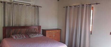 A bedroom with a bed, a wooden nightstand, a wardrobe, and a window with curtains.