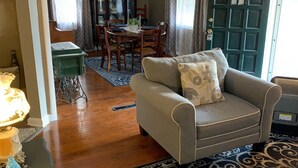 Een woonkamer met een bank, een kamerbreed tapijt met dessin, een eettafel met stoelen en een groene deur.