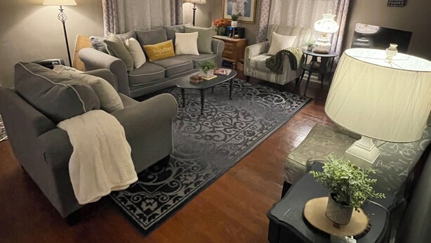 Een woonkamer met een bank, fauteuils, een salontafel, een lamp, een plafondventilator en een vloerkleed.