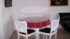 Un coin repas avec une table ronde et quatre chaises blanches, un canapé en cuir noir et deux œuvres d’art encadrées accrochées au mur.