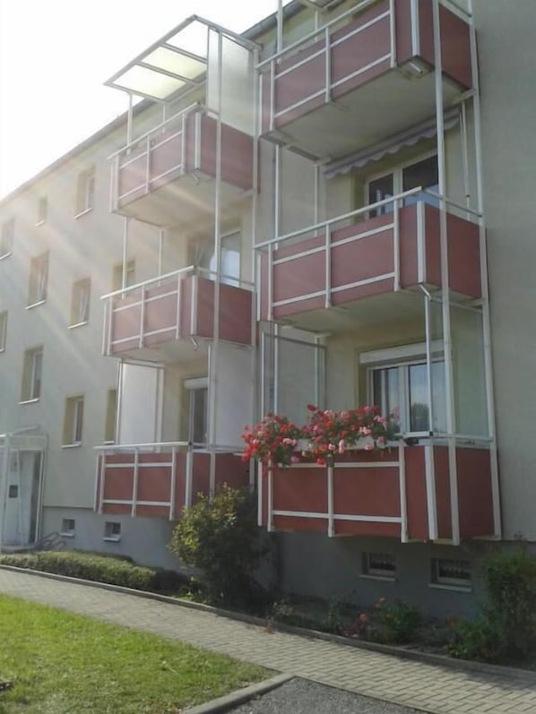 A multi-story residential building with balconies, a gated entrance, and a small garden area.