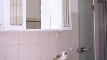 Ein Badezimmer mit einem weißen Waschbecken, einem Spiegel darüber und einer Duschkabine aus Glas.