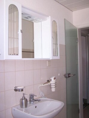 A bathroom with a white sink, a mirror above it, and a glass shower door.