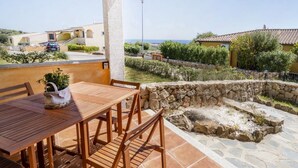 A patio with a wooden table and chairs, a stone wall, and a view of the sea. - Pedra De Oro | 2 Bedroom and Sea View! (Budoni)