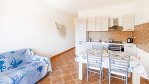 A compact kitchen with white cabinets, a dining table with chairs, and a sofa with a blue pattern. - Pedra De Oro | 2 Bedroom and Sea View! (Budoni)
