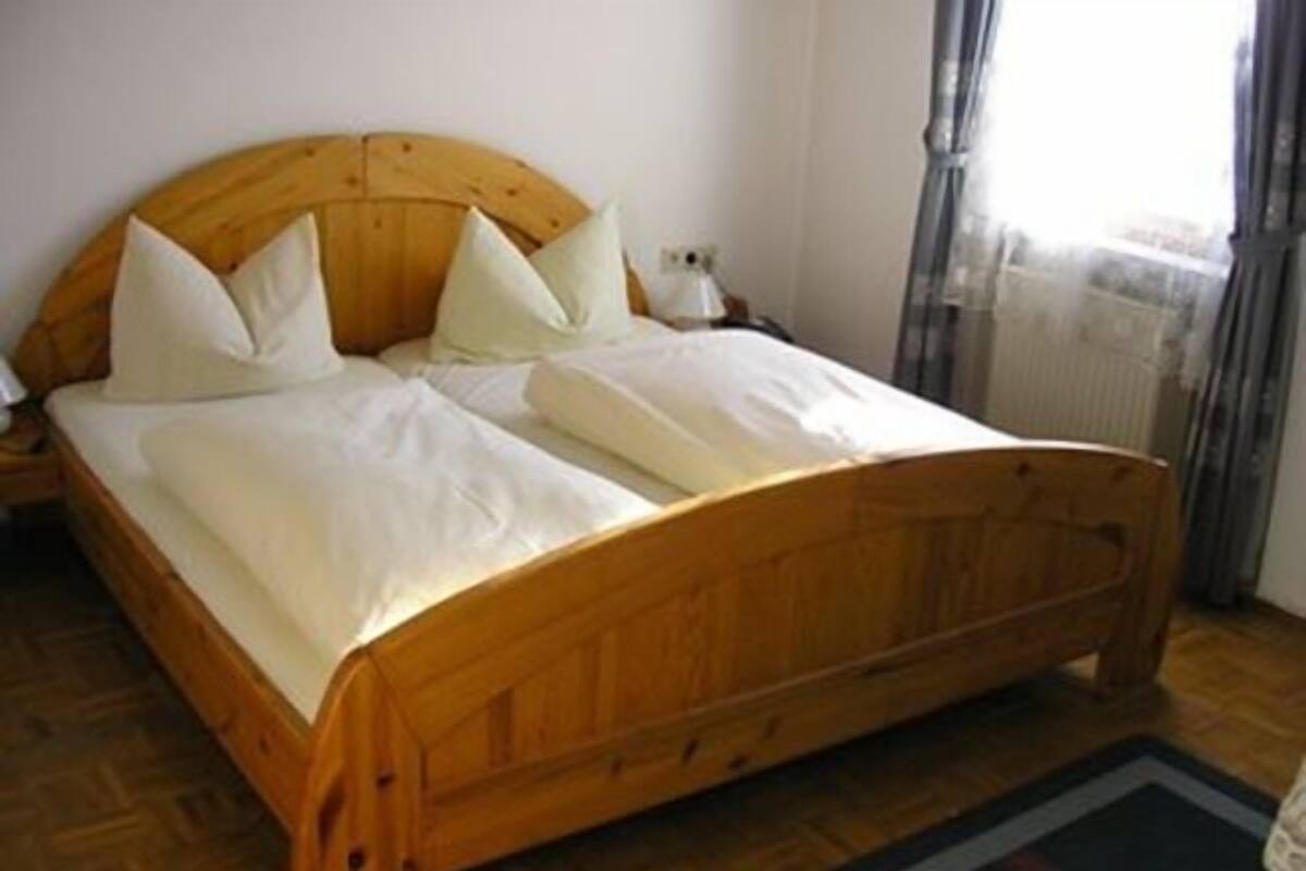 A wooden bed with white bedding in a room with wooden flooring.