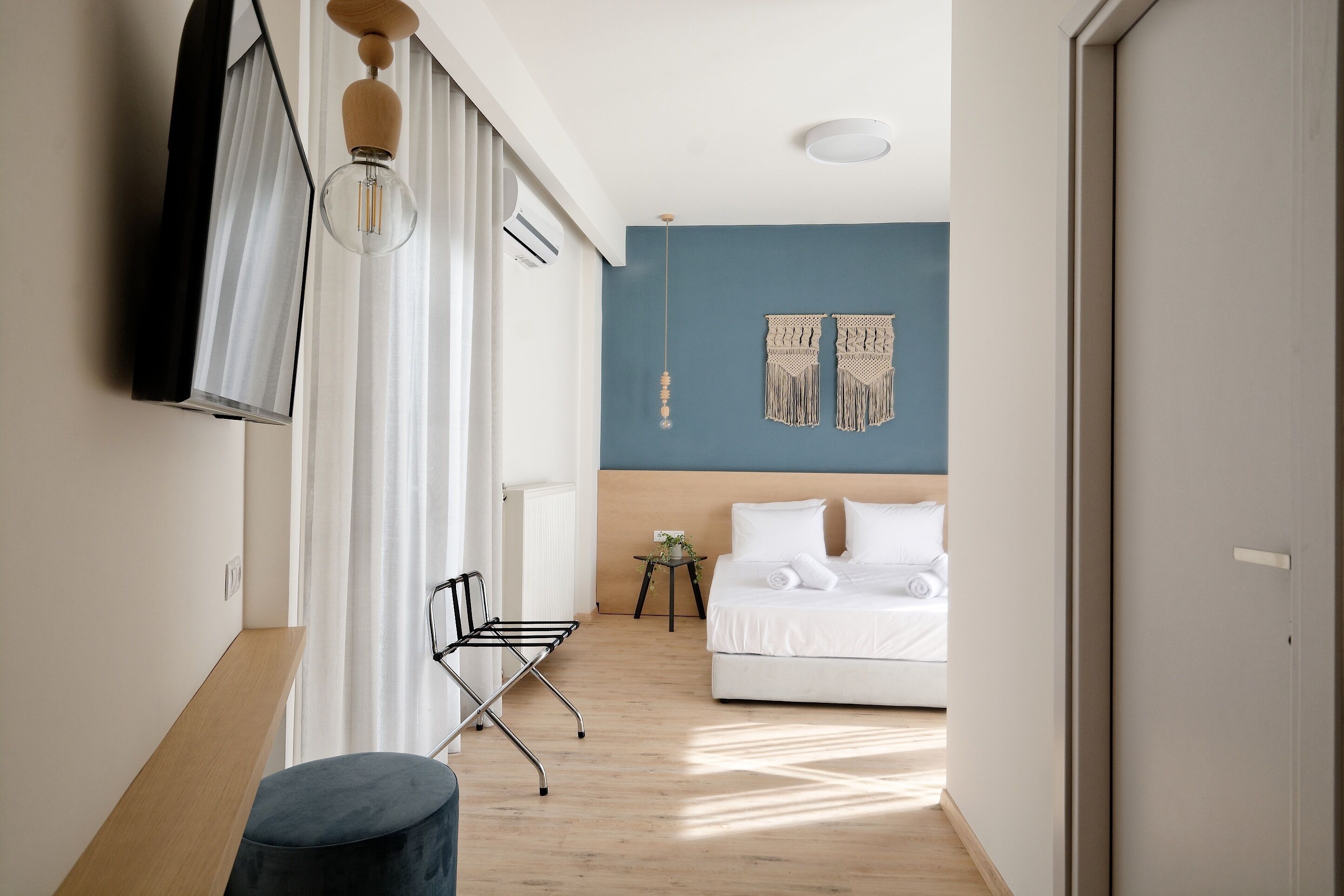 A modern hotel room with a bed, a small bedside table, a chair, and a hanging light fixture.