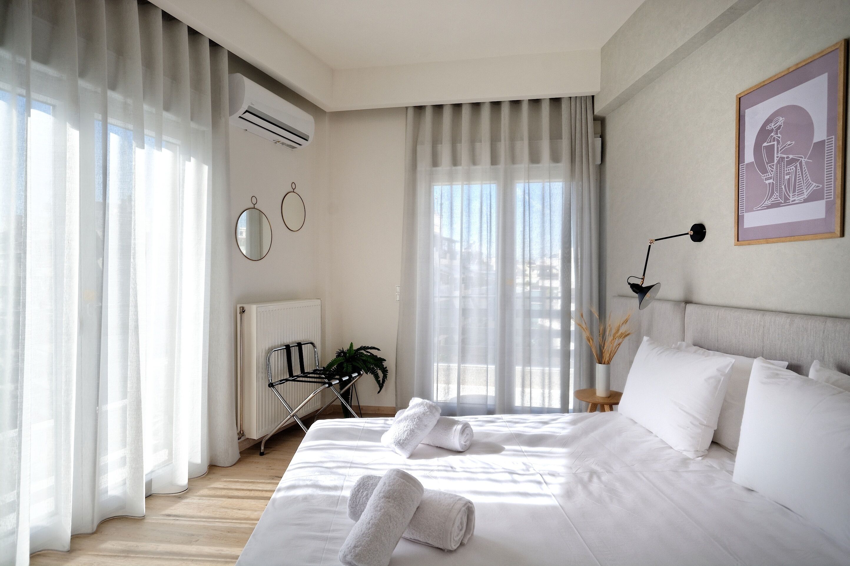 Una habitación de hotel moderna con una cama grande, ropa de cama blanca, un radiador, un escritorio y una ventana con cortinas de gasa.