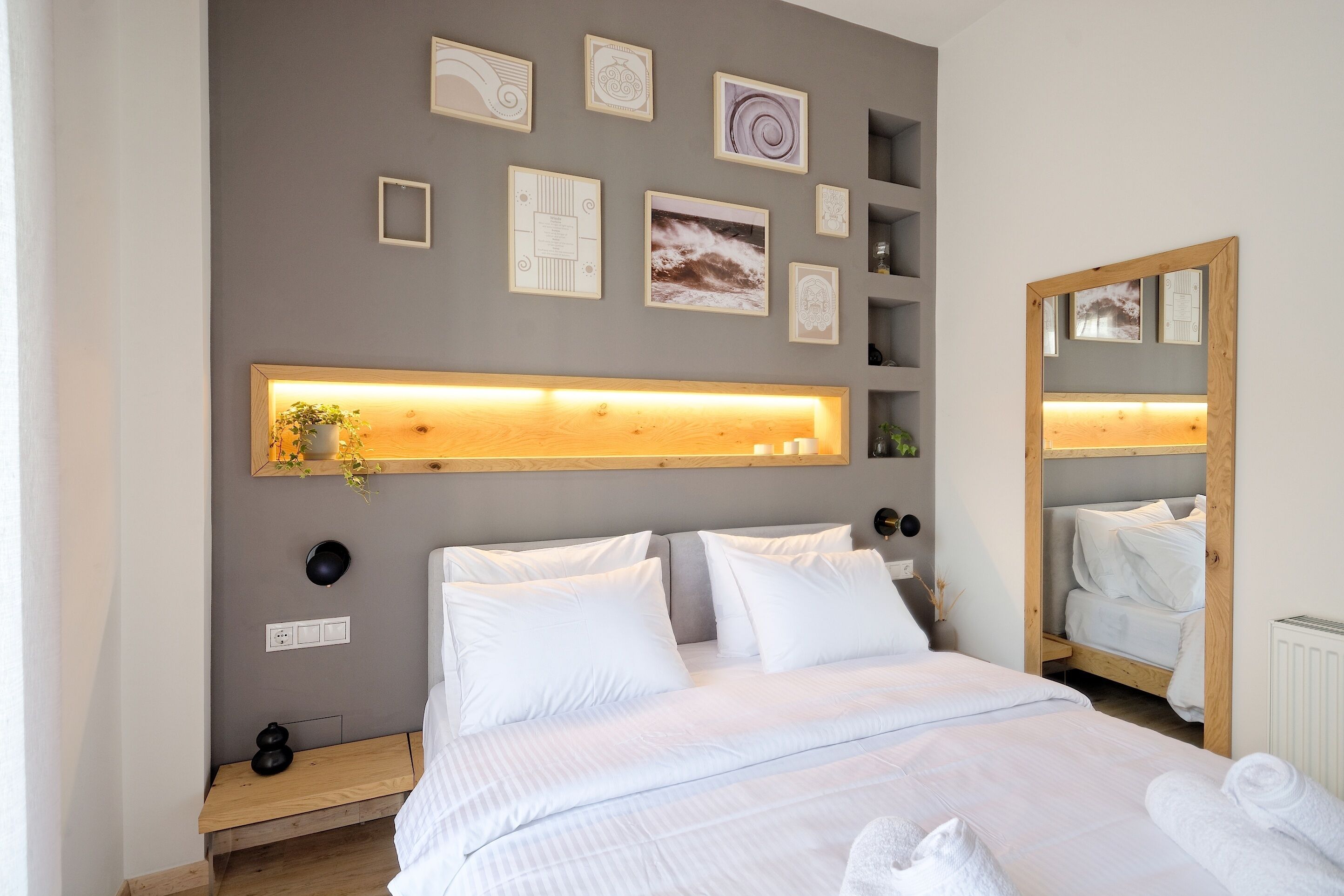 A modern bedroom with a large bed, bedside tables, a mirror, and wall-mounted shelves with decorative items.