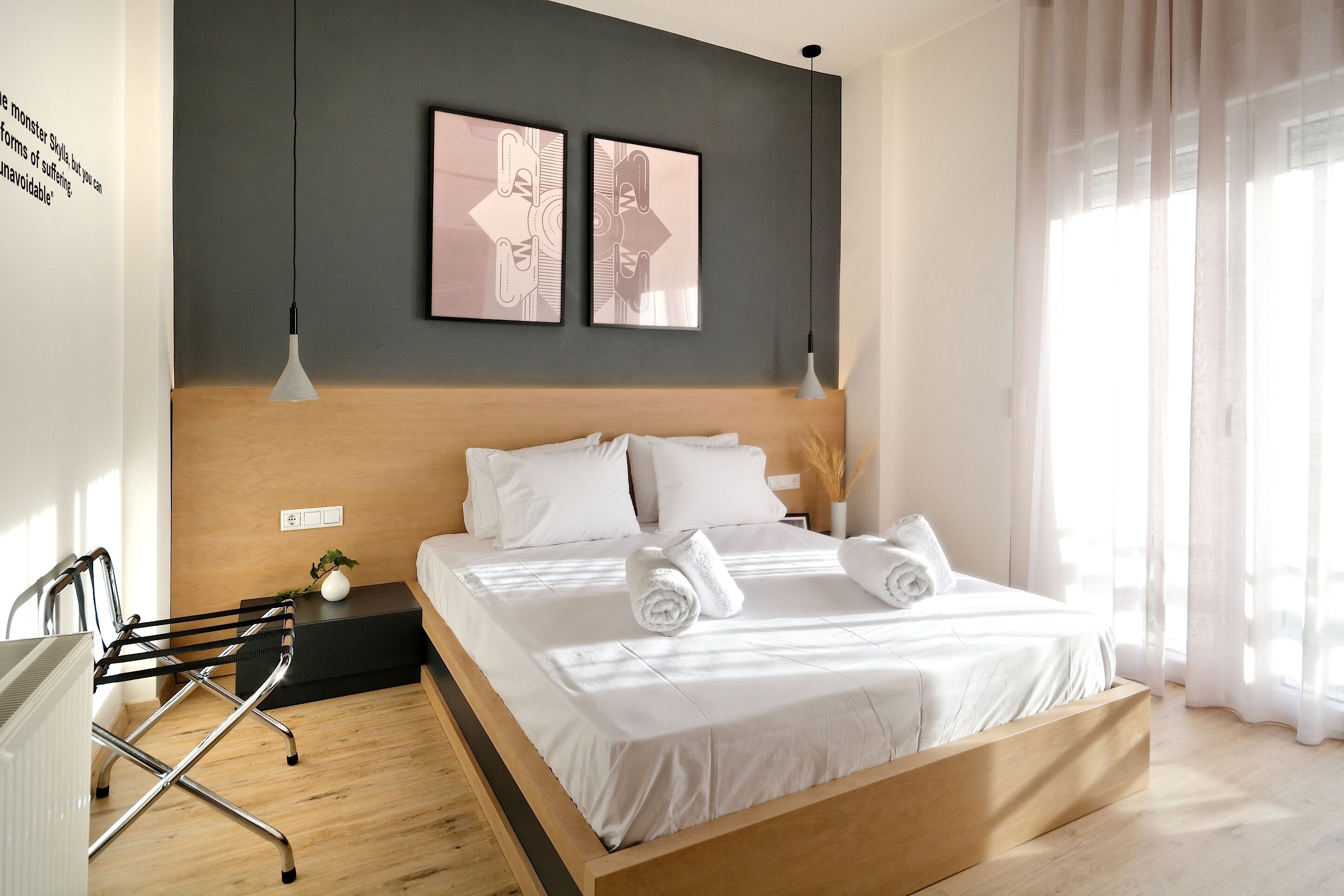 A modern hotel room with a wooden bed, white bedding, and two artwork pieces on the wall.
