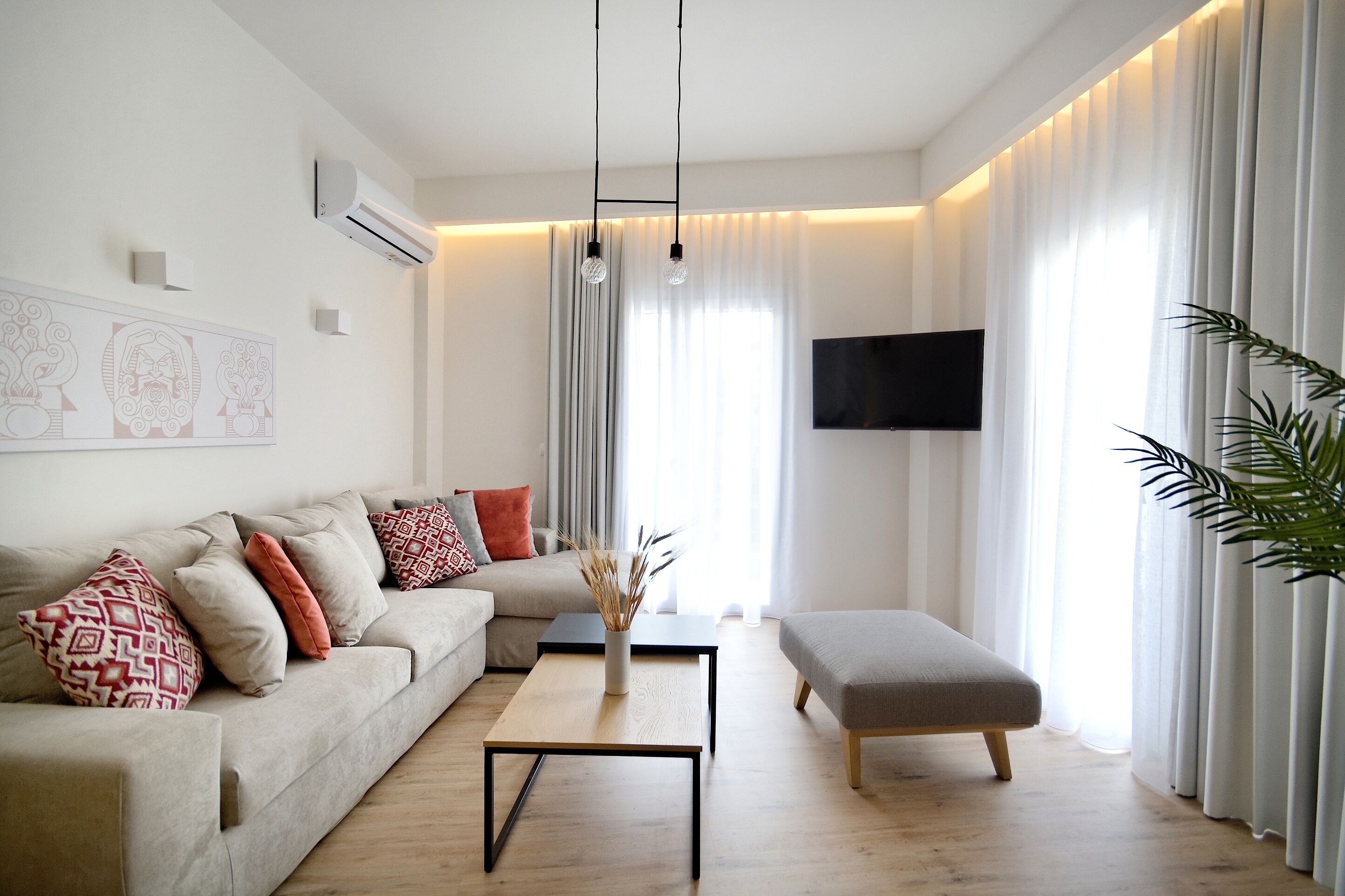 A modern living room with a sofa, ottoman, coffee table, and a flat-screen TV mounted on the wall.