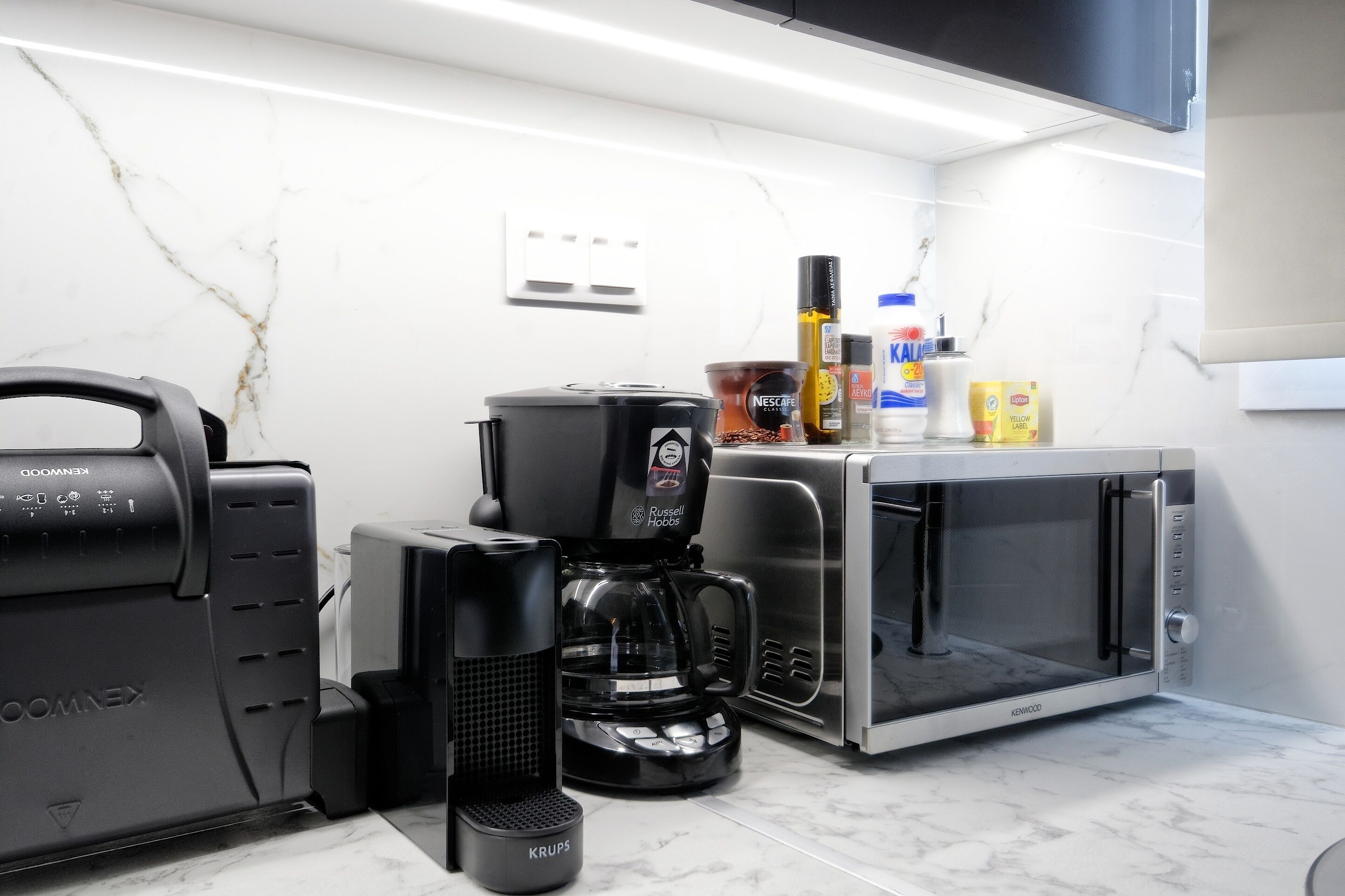 A modern kitchen with a Kevo coffee maker, a Krups coffee grinder, a Nescafe coffee pot, and a microwave.