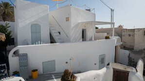 Un bâtiment blanc avec un escalier, une petite porte et une poubelle jaune.