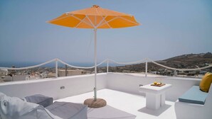 Une terrasse sur le toit avec un canapé blanc, une petite table sur laquelle est posé un panier de fruits et un parasol orange.