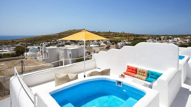 Una piscina sul tetto con un ombrellone giallo, pareti bianche e cuscini colorati.