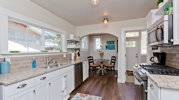 A modern kitchen with white cabinets, granite countertops, a dishwasher, a stove, and a dining area with a table and chairs.