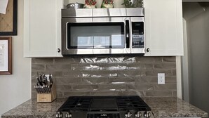 A kitchen with a stainless steel stove, a microwave, and a brick backsplash.