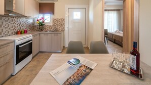 A compact kitchen with a stove, oven, and a dining area with a table set for a meal. - Nancy's Luxury Apartments (Zakynthos)