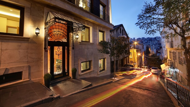 A building with a prominent entrance, a balcony with railings, and a street with moving lights. - The Fox Hotel (Istanbul)