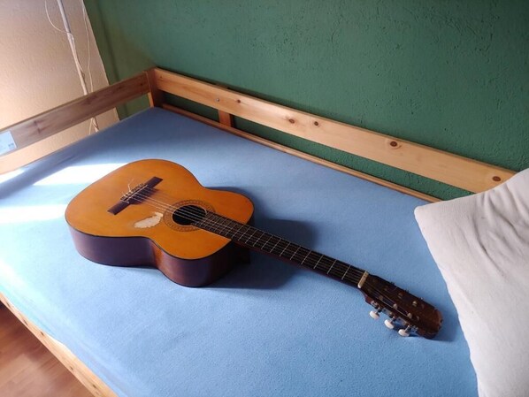 Una guitarra sobre una cama con un colchón azul y una pared verde al fondo.