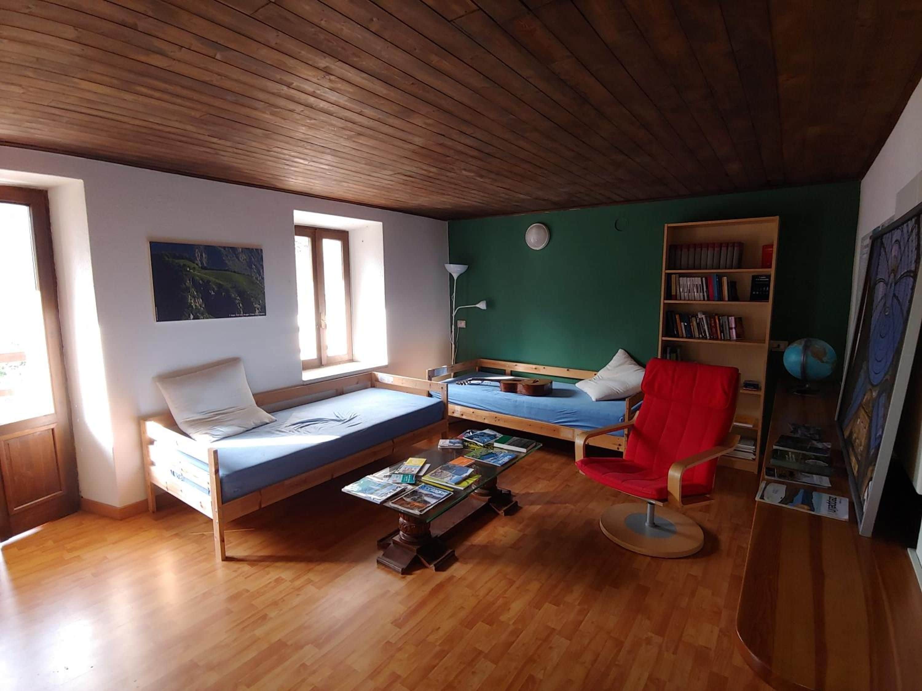 Una stanza con un letto, una sedia rossa, una libreria e una finestra.