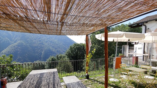 Un espace extérieur aménagé avec des tables et des chaises en pierre, une tonnelle en bambou et une vue sur un paysage montagneux.