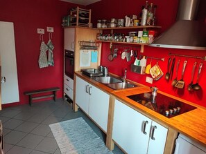 A kitchen with white cabinets, a wooden countertop, and a red wall. - Ostello Val Grande (Cossogno)