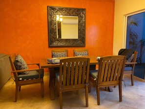 A dining area with a wooden table and chairs, a large mirror on the wall, and an orange wall. - Casa Estrellas - private pool, amazing roof top view, and walk to local beach (Cabo San Lucas)