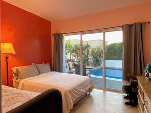 A hotel room with a bed, a desk, a chair, and a view of a swimming pool and greenery. - Casa Estrellas - private pool, amazing roof top view, and walk to local beach (Cabo San Lucas)