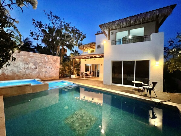 A modern two-story house with a swimming pool, outdoor seating, and a stone wall.