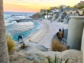 A beach with a rocky shoreline, a barbecue grill, and a building with a balcony overlooking the ocean.