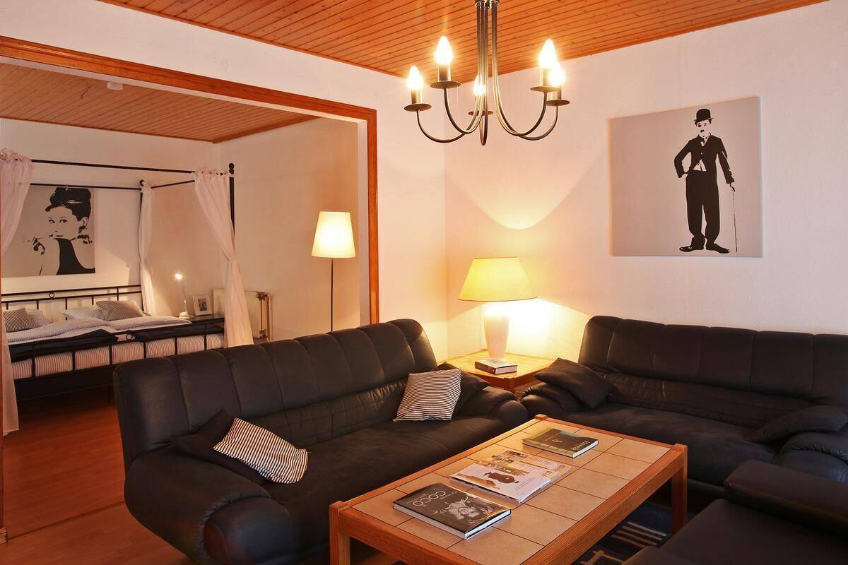 Un salon moderne avec deux canapés en cuir foncé, une table basse en bois sur laquelle sont posés des magazines, un lustre et un lit à baldaquin.