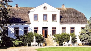 A white building with a symmetrical facade, a central entrance, and a gravel driveway. - Feriengut Neuhof (Fehmarn)