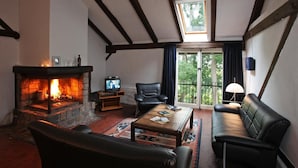 A cozy living room with a stone fireplace, leather furniture, and a balcony with a view. - Feriengut Neuhof (Fehmarn)