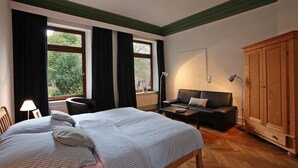 A bedroom with a large bed, a sofa, a wooden wardrobe, and a window with curtains. - Feriengut Neuhof (Fehmarn)