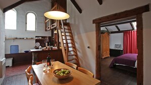A cozy dining area with a wooden table, chairs, and a basket of apples. A wooden ladder and a staircase are visible in the background, leading to an upper level. - Feriengut Neuhof (Fehmarn)