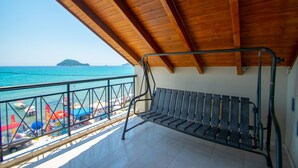 Ein Balkon mit Holzboden, der auf einen Strand mit bunten Sonnenschirmen und eine ferne Insel blickt.