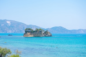 A coastal landscape with a prominent rock formation surrounded by clear blue water, a pier, and distant mountains. - George Apartments (Zakynthos)