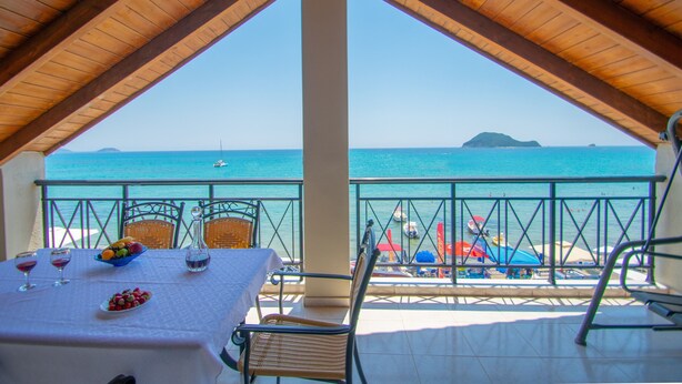 Eine Terrasse mit Esstisch, mit Blick auf einen Strand mit Sonnenschirmen und Booten.
