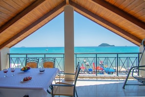 A terrace with a table set for dining, overlooking a beach with umbrellas and boats. - George Apartments (Zakynthos)