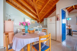 A dining area with a round table, chairs, a vase with flowers, and a kitchen in the background. - George Apartments (Zakynthos)