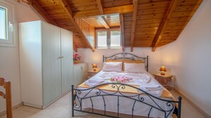 Ein Schlafzimmer mit Holzbalkendecke, einem Bett mit weißen Bettwäsche, zwei Nachttischen mit Lampen und einem Kleiderschrank.