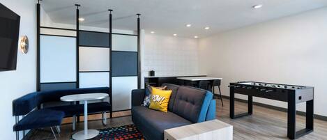 A modern living room with a sofa, a coffee table, a foosball table, and a patterned rug.