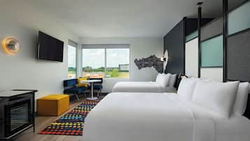 A modern hotel room with a large bed, a desk, a TV, and a view of the city.